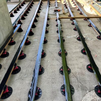 Lambourdes sur plots réglables noirs et rouges pour l'installation d'une terrasse en bois sur dalle béton.