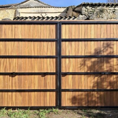 Portail battant moderne en bois avec cadre métallique noir devant un mur en vieilles pierres.