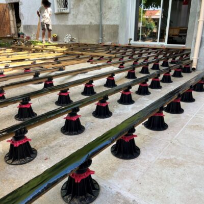 Lambourdes sur plots réglables installées sur une dalle béton pour la structure d'une terrasse en bois.
