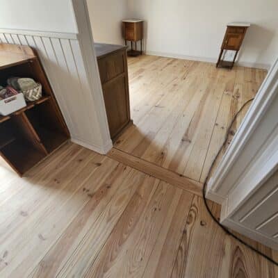 Parquet en bois clair d'une pièce lumineuse avec meubles anciens et murs blancs.