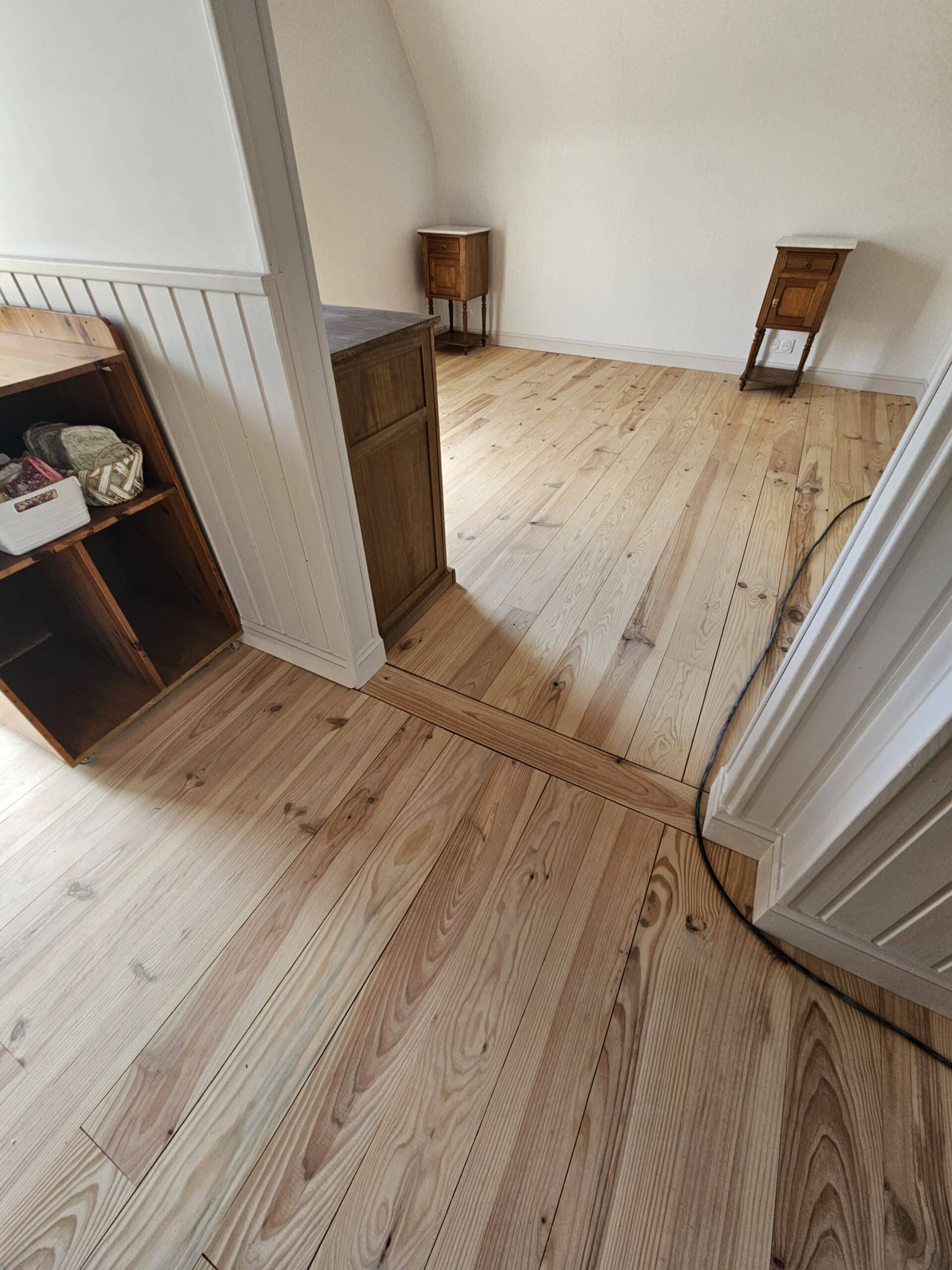 Parquet en bois clair d'une pièce lumineuse avec meubles anciens et murs blancs.
